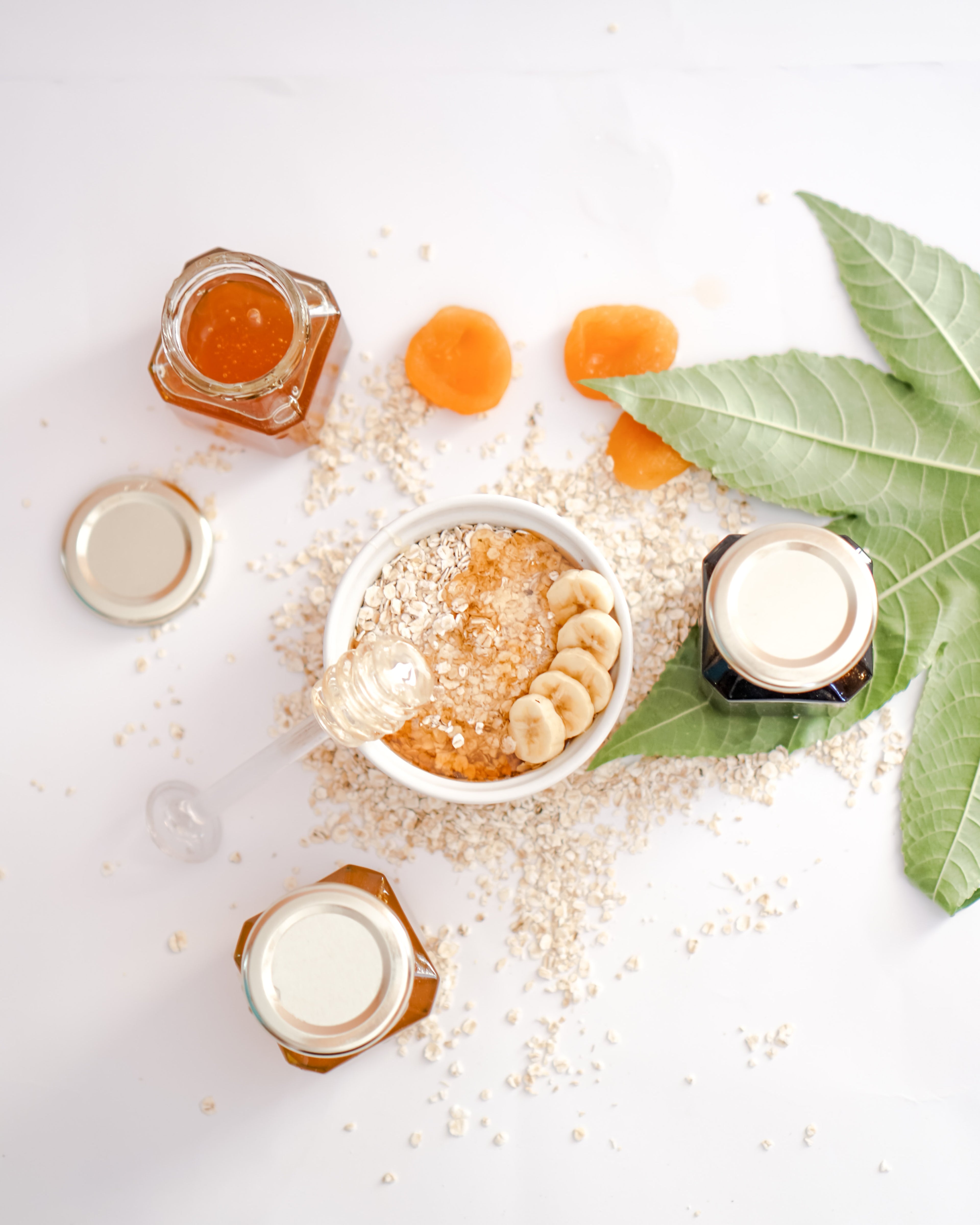 Table with Honey jars, honey stick and grains scattered with a green leaf